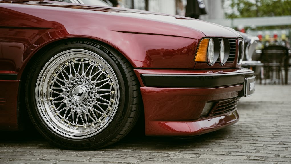 BMW M5 E34: The Hand-Built M5 4 Close-up of a classic red BMW E34 with polished wheels in an urban setting showcasing automotive style.