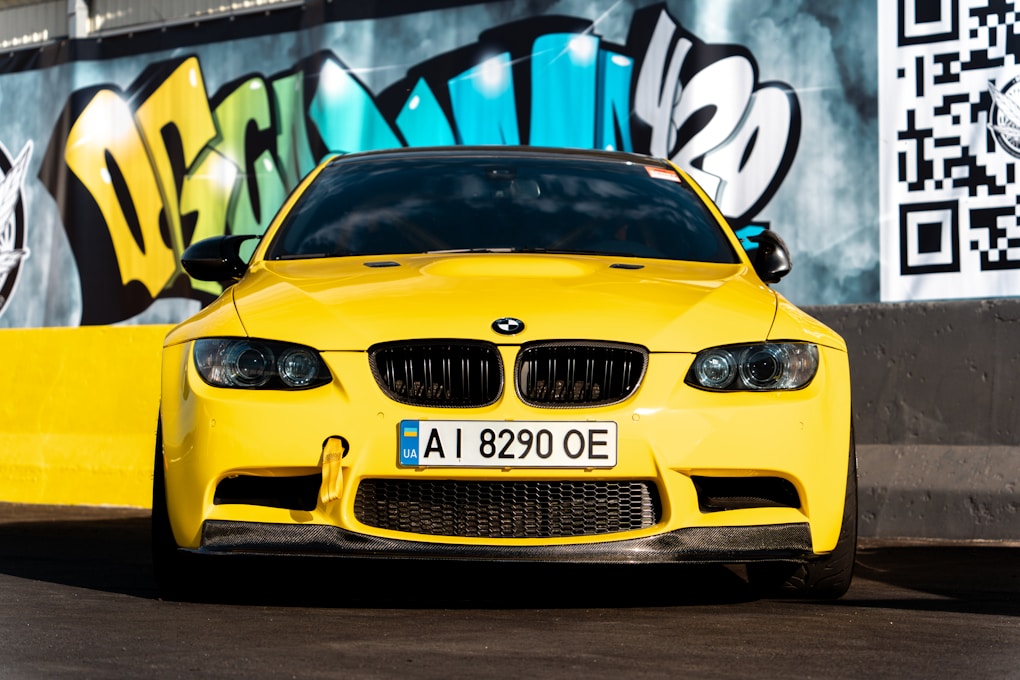 A yellow car parked in front of a graffiti covered wall