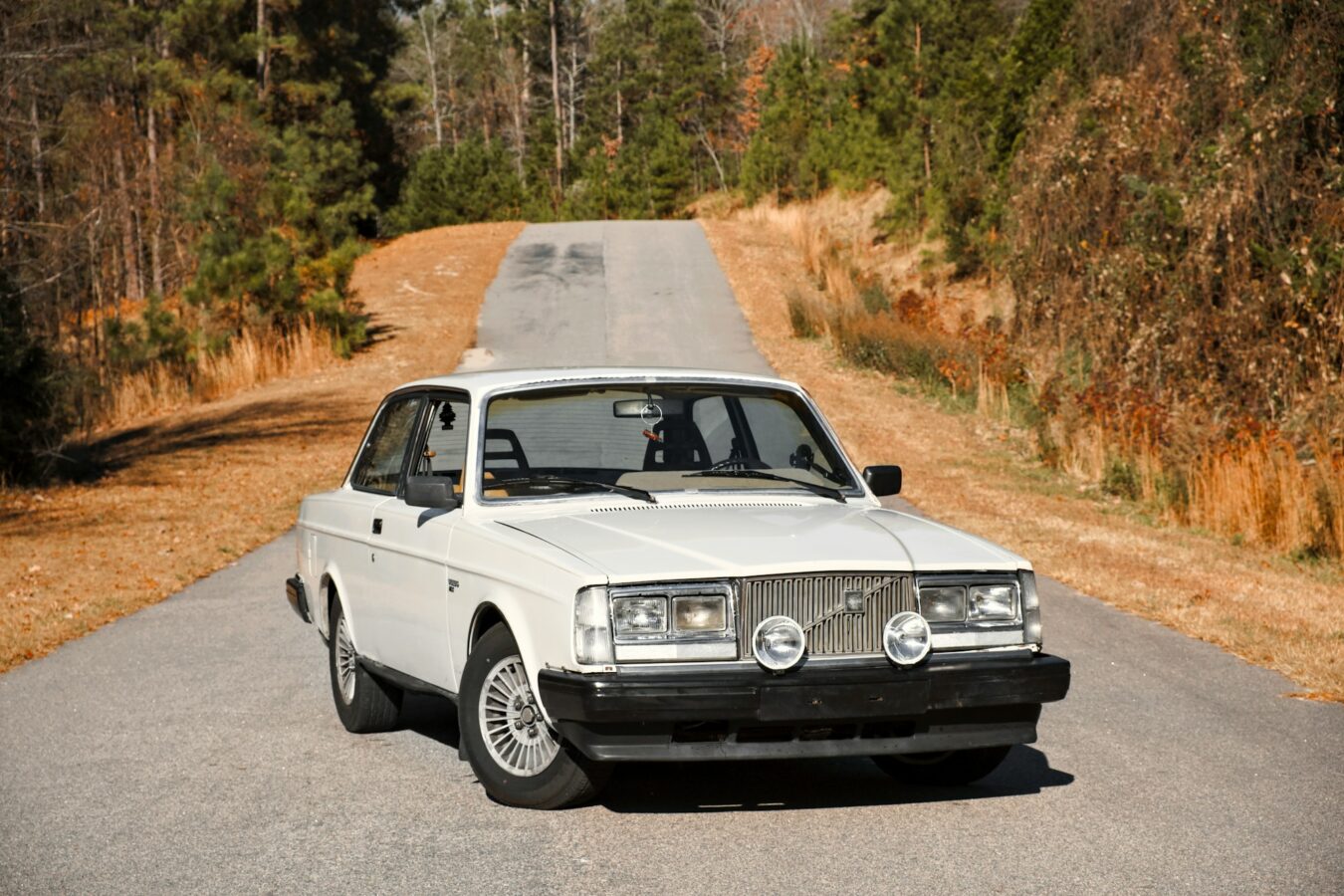 a white volvo 240 parked on the side of a road