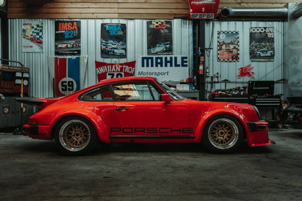 Red porsche sports car parked in a garage with posters on the wall